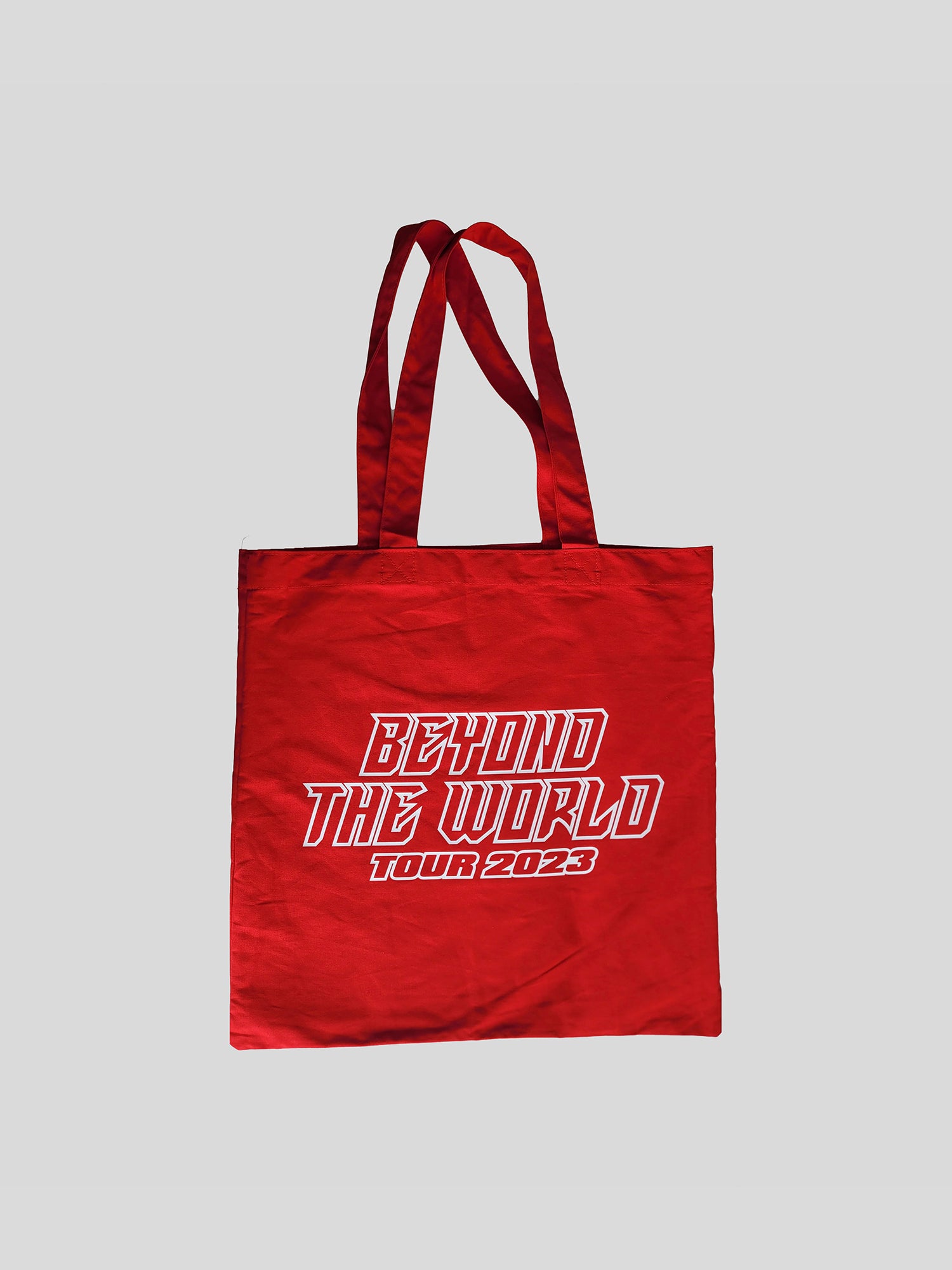 Rückansicht der gleichen roten Tragetasche mit auffälligem weißem Aufdruck „BEYOND THE WORLD TOUR 2023“ in kantiger, versetzter Typografie.