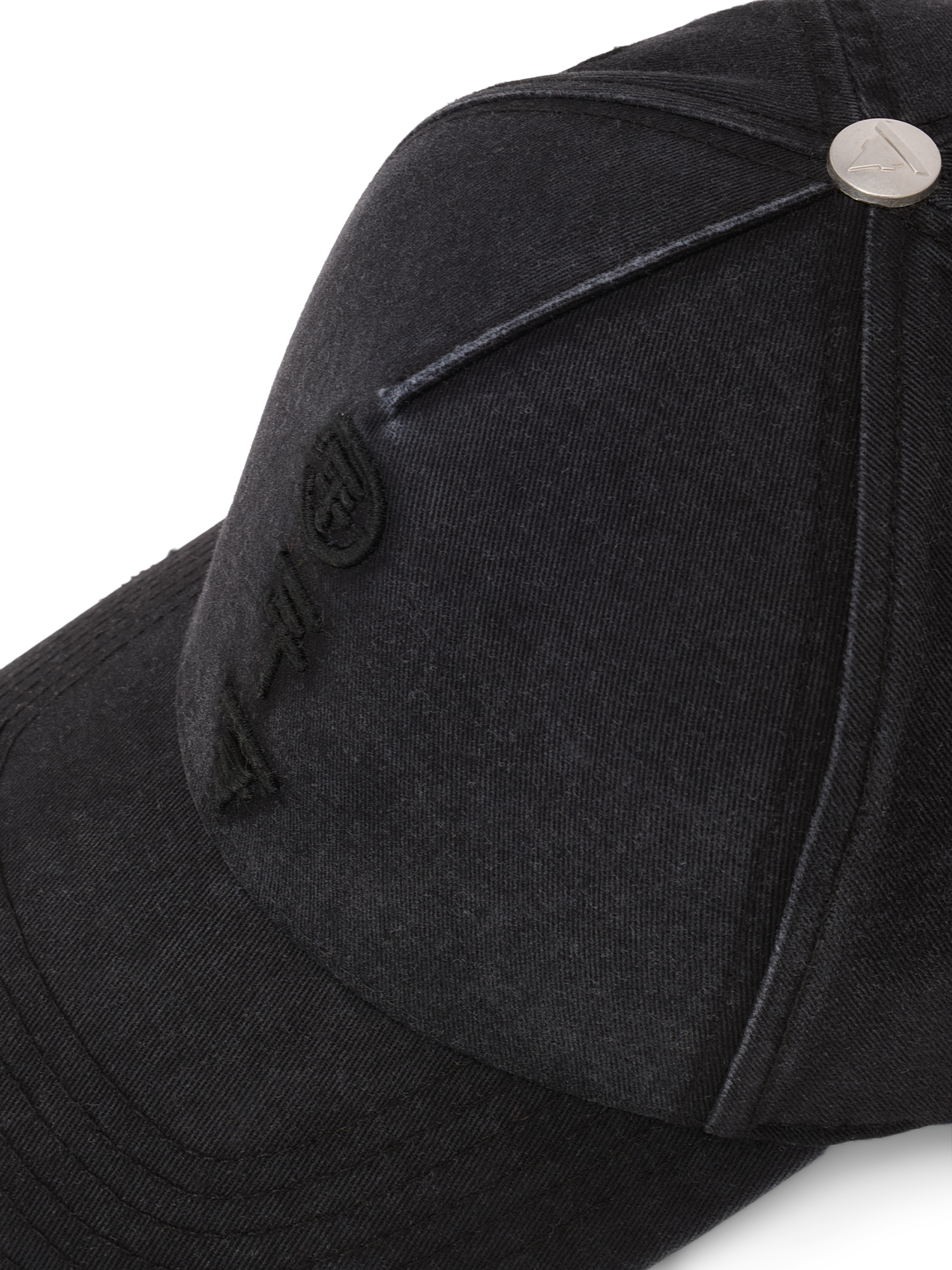 Nahaufnahme der schwarzen Baseballcap mit geprägtem Metallknopf oben und gestickten Tokio Hotel Symbolen auf der Front.