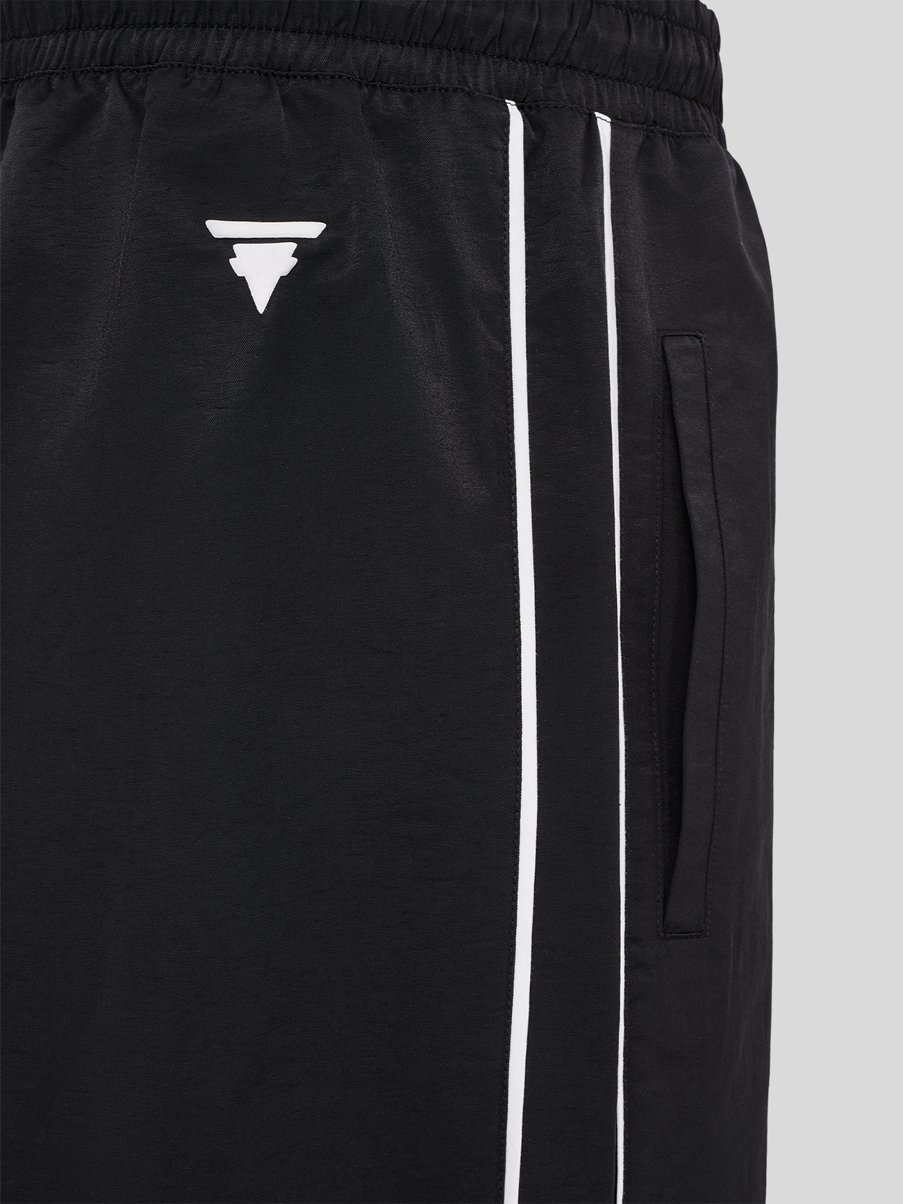 Nahaufnahme des weißen Logos und der seitlichen Eingrifftasche auf schwarzem Stoff mit weißen Zierstreifen.