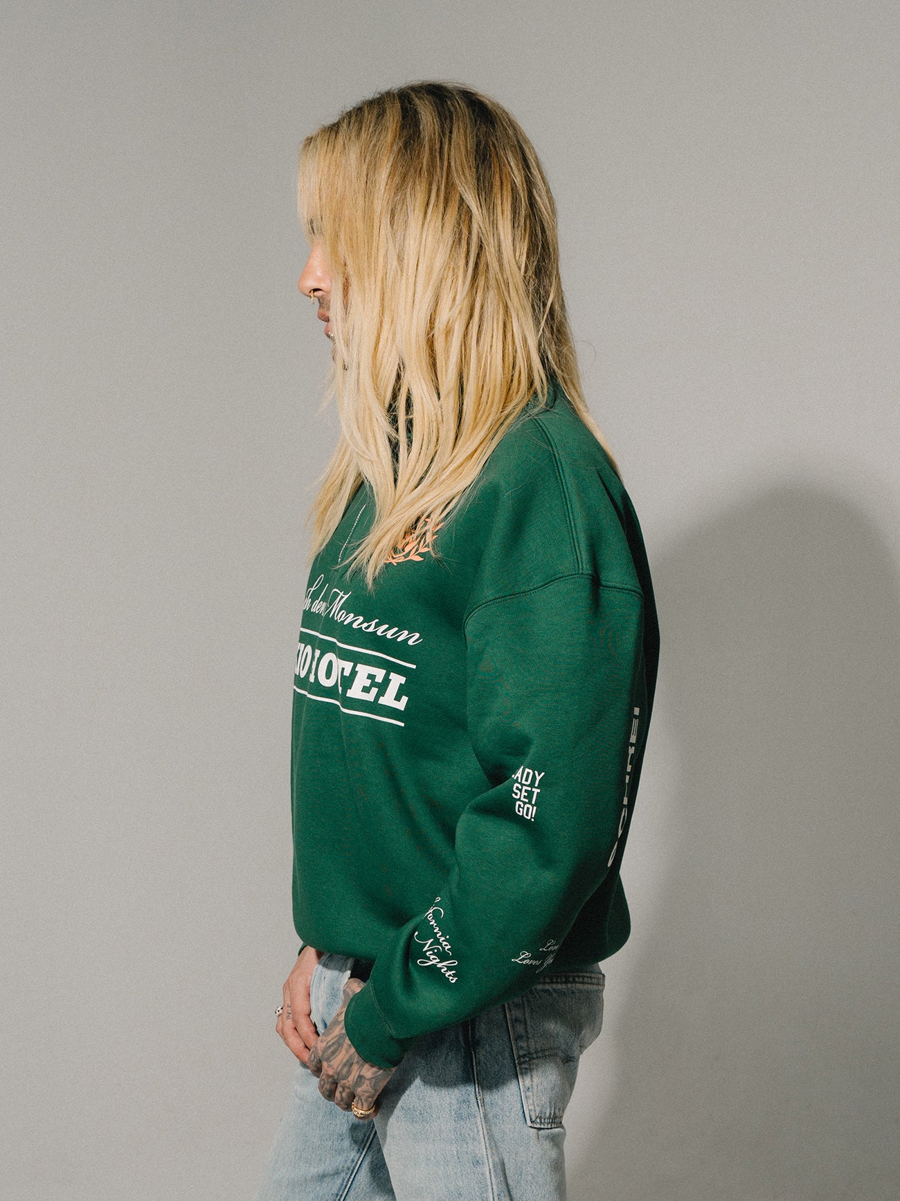 Seitenansicht einer Person im grünen Sweater mit Ärmel-Prints wie „Ready Set Go!“ und „California Nights“.