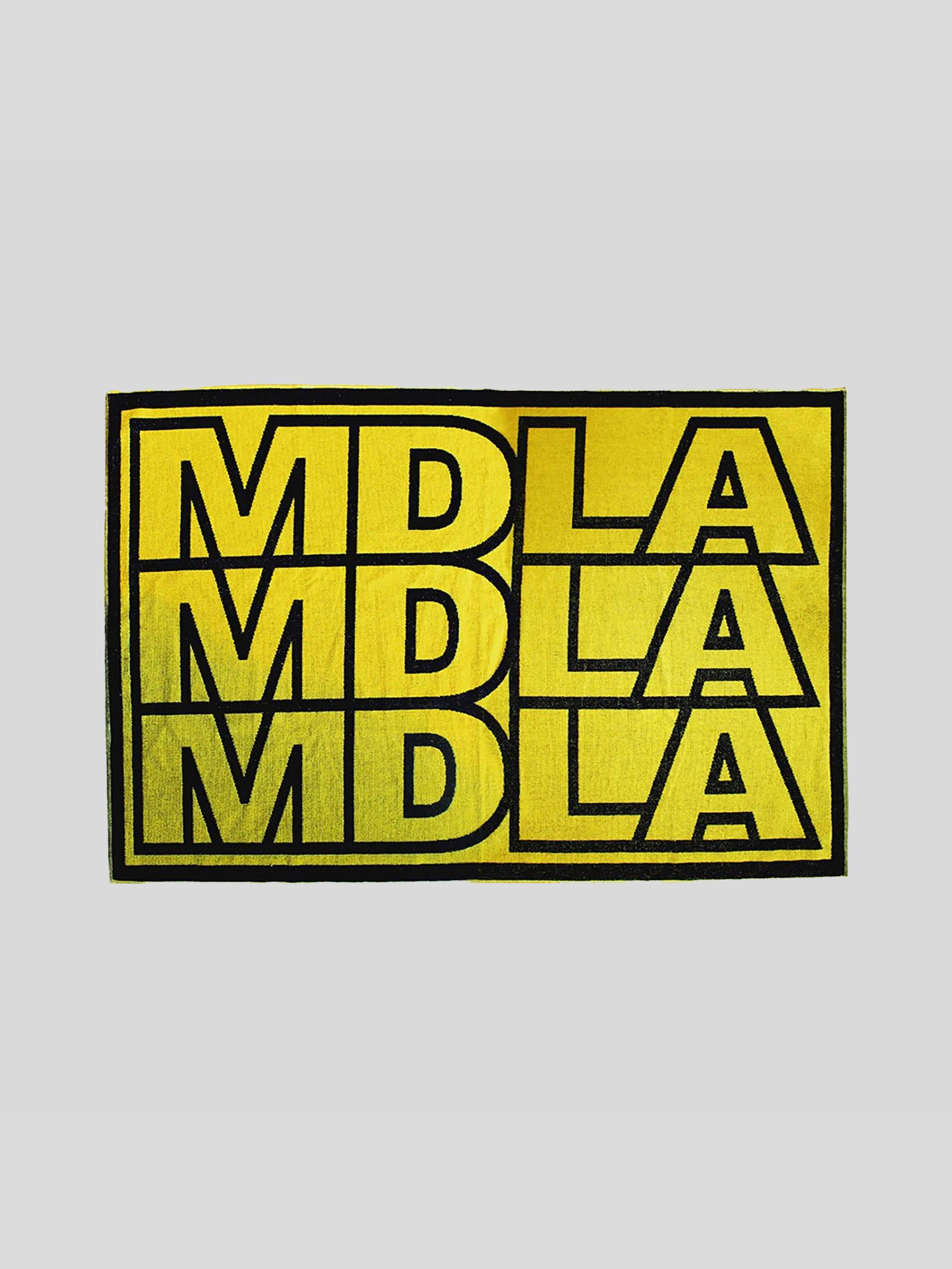 Flach ausgebreitetes Handtuch mit markantem Allover-Schriftzug „MDLA“ in drei Reihen. Schwarze Buchstaben auf intensiv gelbem Grund, eingefasst von einem breiten schwarzen Rahmen.