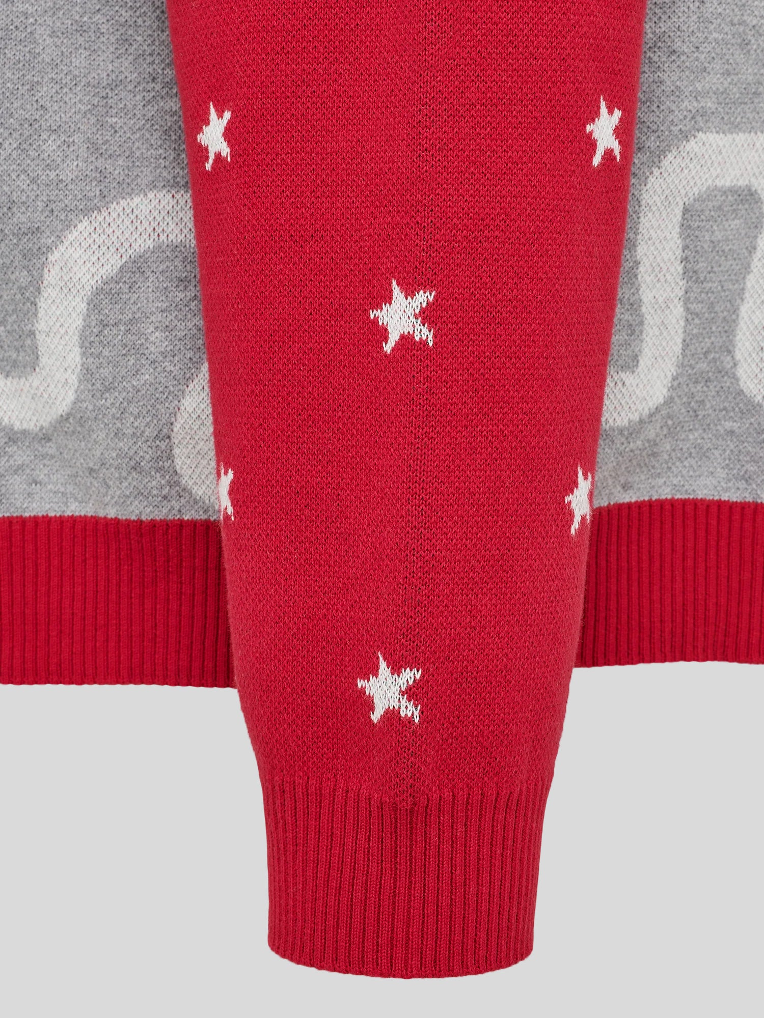 Nahaufnahme des roten Strickärmels mit kleinen weißen Sternmotiven und breitem Rippbündchen. Im Hintergrund erkennt man den grau-melierten Rumpfbereich des Pullovers.