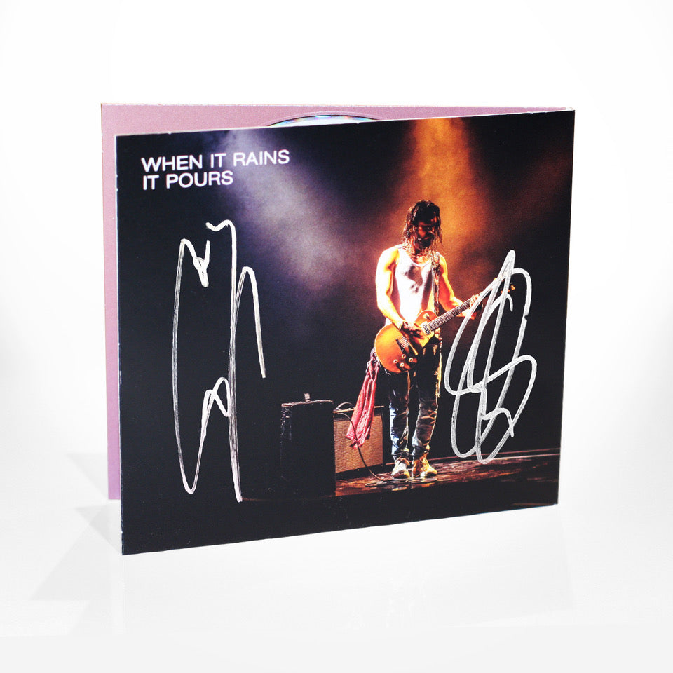 Quadratisches CD-Cover mit einem Foto von Tom Kaulitz auf der Bühne mit Gitarre, Lichtstrahl von oben. Links der weiße Text „WHEN IT RAINS IT POURS“. Zwei silberne Autogramme sind auf dem Cover unterschrieben.
