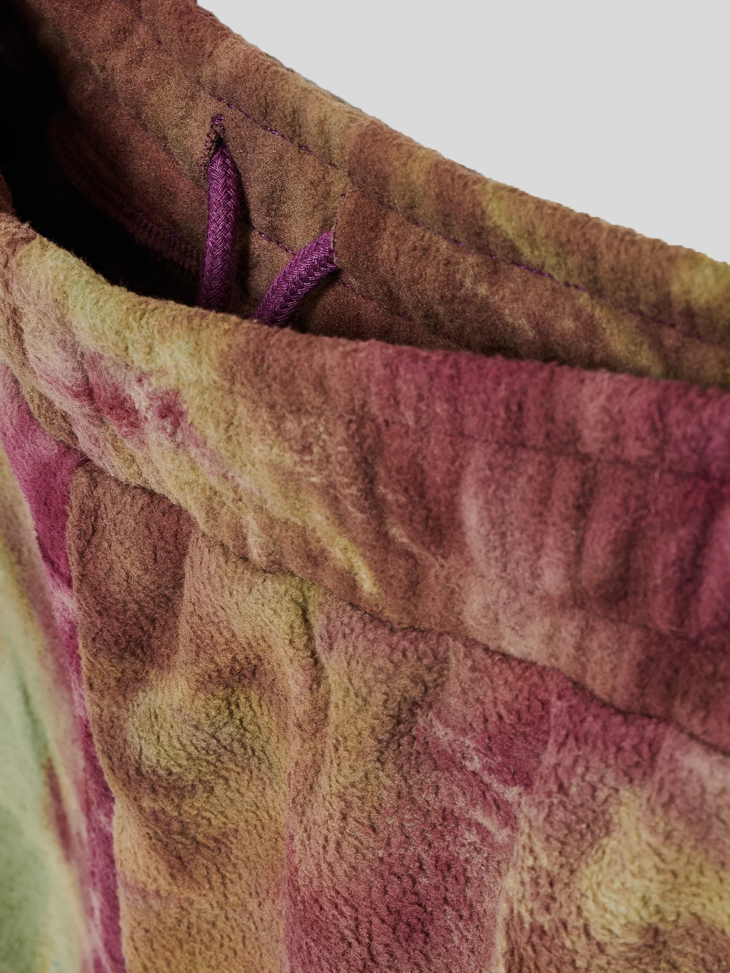 Nahaufnahme des elastischen Hosenbunds einer Batik-Fleecehose in Bordeaux-, Braun- und Grüntönen. Sichtbar ist ein violettfarbener Tunnelzug zur Weitenregulierung im Inneren des Bundes.