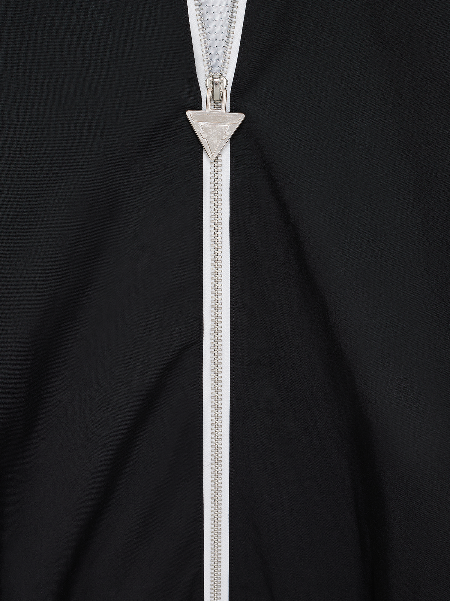 Nahaufnahme des silbernen, dreieckigen Reißverschlussanhängers mit graviertem Tokio Hotel Logo.