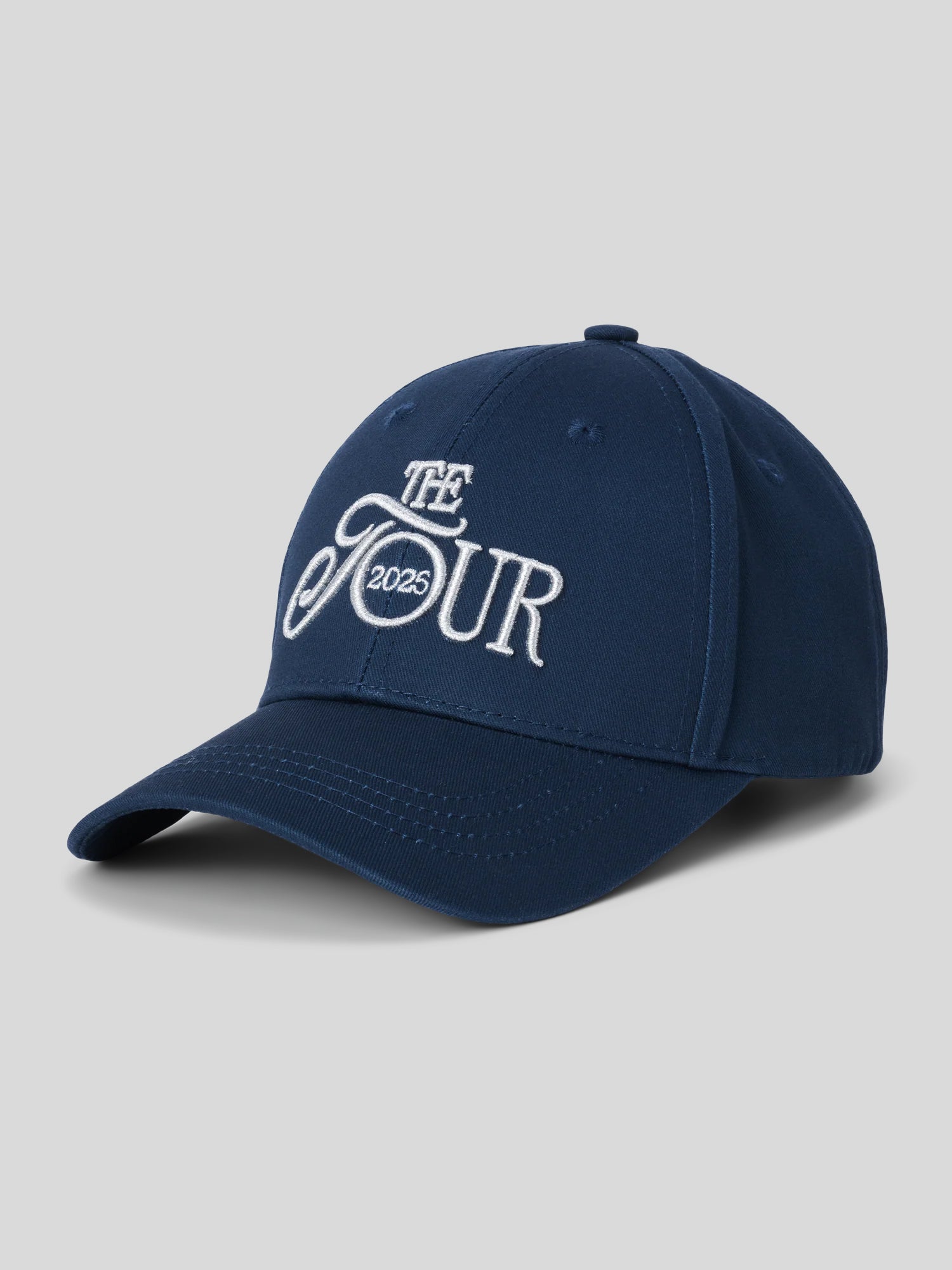 Dunkelblaue Baseballcap mit gebogenem Schirm und weißer Stickerei auf der Front: „THE TOUR 2025“ in einer Kombination aus verschnörkelter und klarer Schrift.