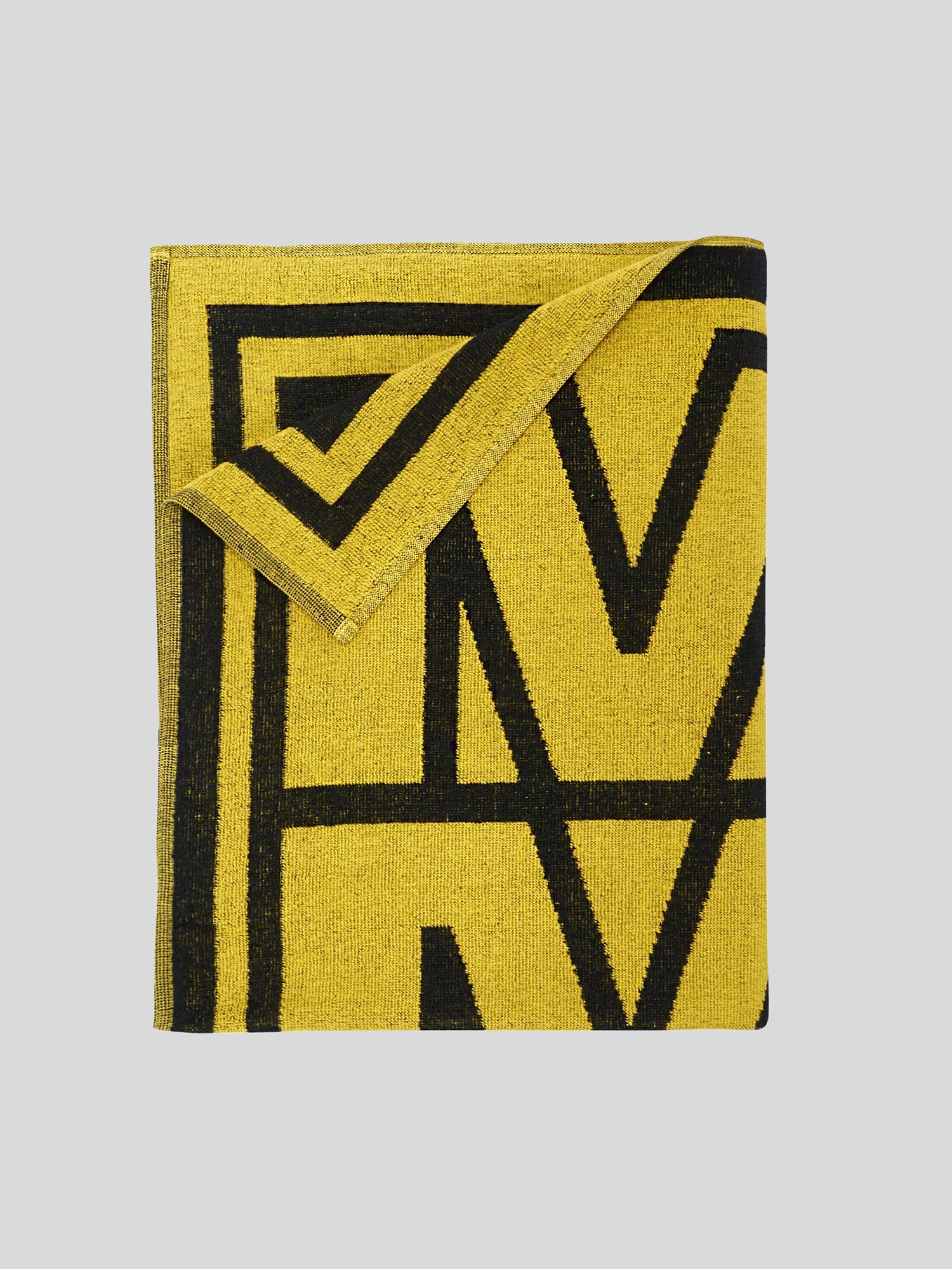 Gefaltetes Handtuch in Gelb mit schwarzem grafischem Muster, bei dem eine Ecke elegant nach vorne umgeschlagen ist. Großformatiger „MDLA“-Schriftzug ist teils sichtbar.
