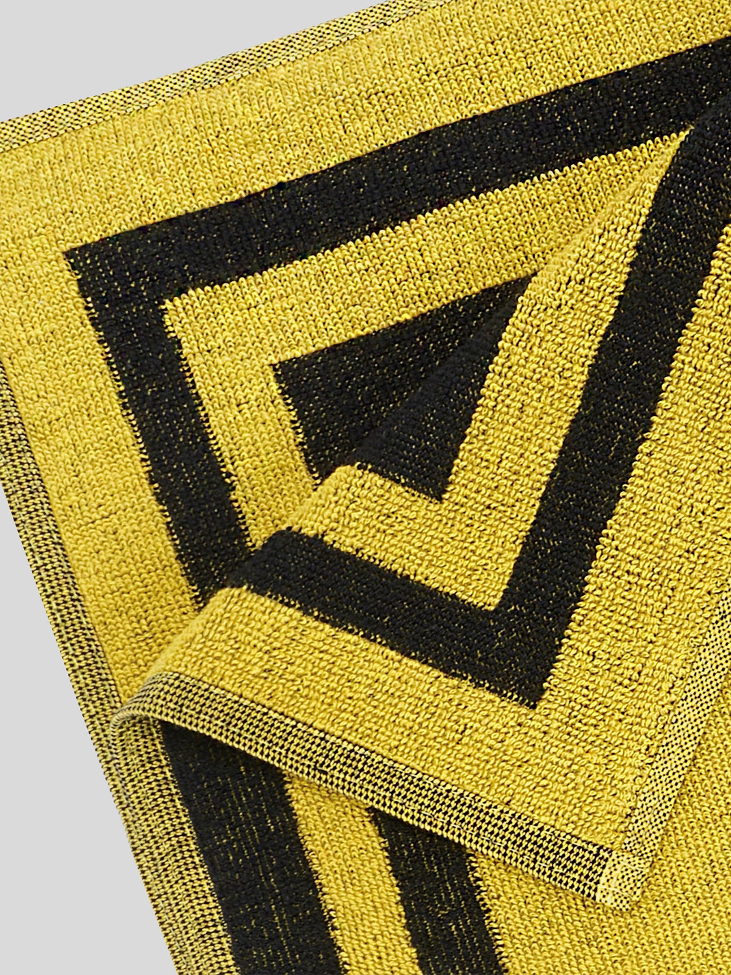 Nahaufnahme der Webstruktur und Kante des Handtuchs. Der kräftige Schwarz-Gelb-Kontrast betont das kantige MDLA-Muster und die hochwertige Verarbeitung.