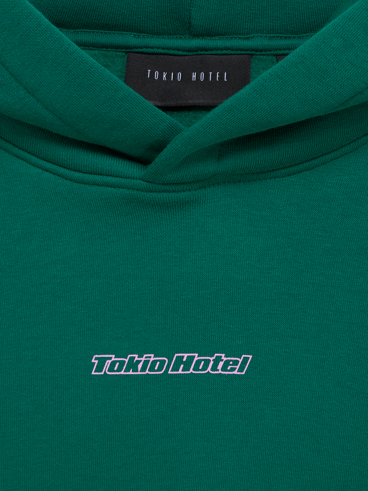 Detailansicht des Brustprints mit dem Tokio-Hotel-Schriftzug in Rosa und dem Innenlabel im Nackenbereich, auf dem ebenfalls „Tokio Hotel“ steht.