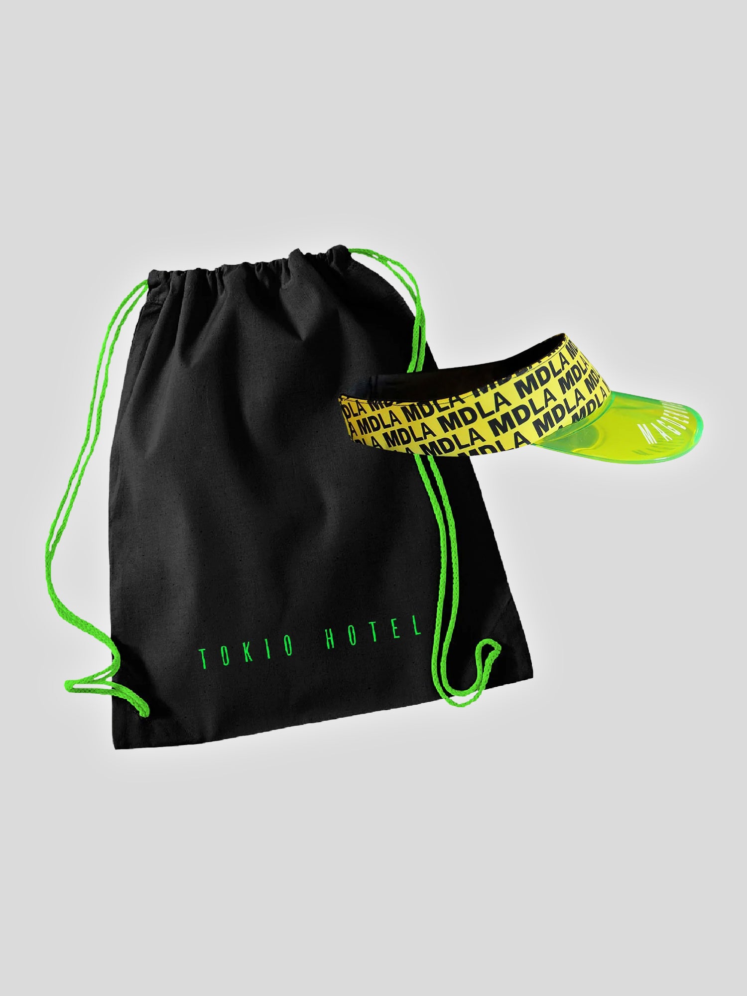Schwarzer Turnbeutel mit neon-grünen Kordeln und dem Aufdruck „TOKIO HOTEL“ in grüner Schrift. Daneben liegt ein Sonnenschild mit gelbem, halbtransparentem Schirm und schwarzem Band, das mehrfach mit dem Schriftzug „MDLA“ in Schwarz auf Gelb bedruckt ist.